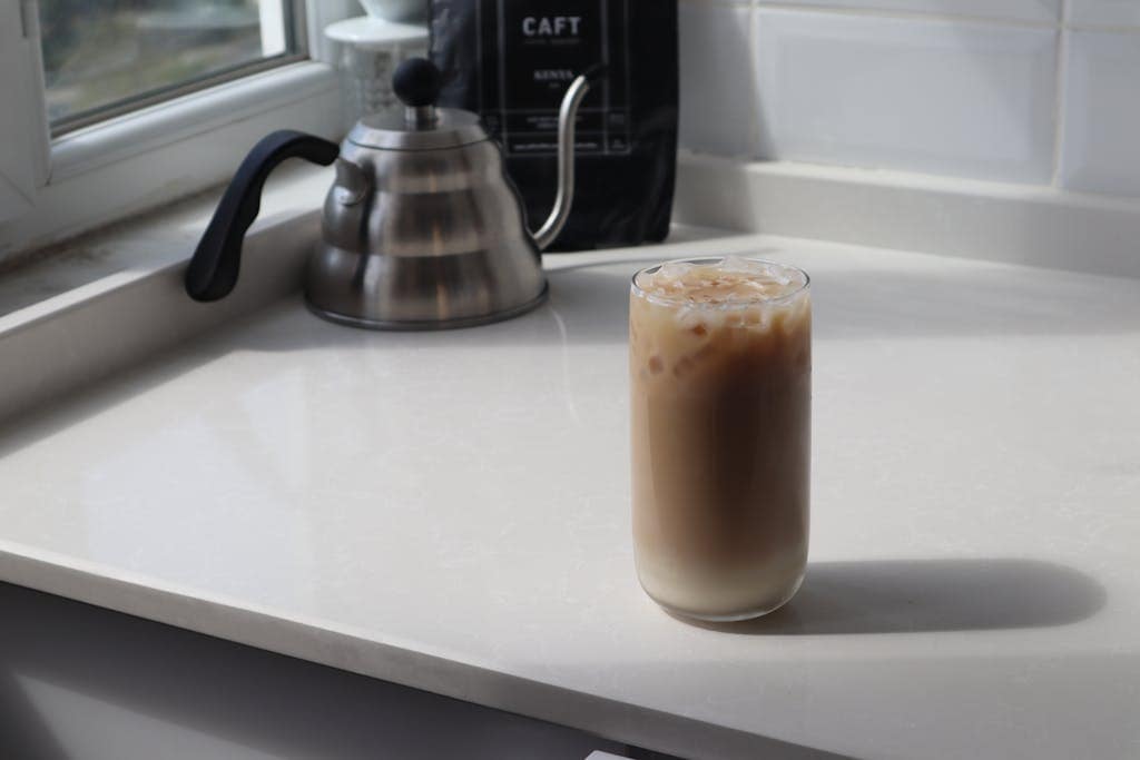 Best Coffee Beans for Cold Brew: Top Picks 5 High angle glass of delicious iced latte and metal coffee kettle placed on white table in kitchen