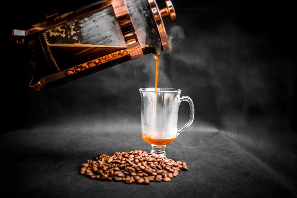 Aeropress vs French Press: Which Brews the Best Cup? 21 Aromatic hot coffee being poured from French press into elegant glass with pile of coffee beans beside on black background