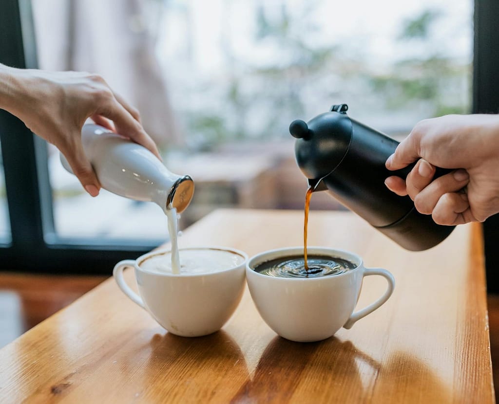 Person Pouring Milk on White Ceramic Cup